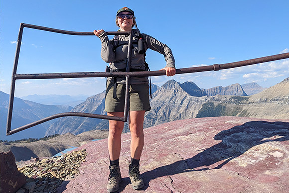 A ranger holding a large metal sign post with mountains in the background.