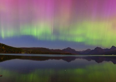 Pink and green northern lights dance above mountains and a lake.