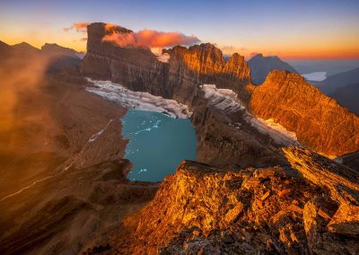 Sunrise on mountain ridge with a glacier and lake below.
