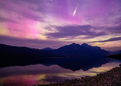 A comet shoots across the sky with purple aurora in the background and mountains below.