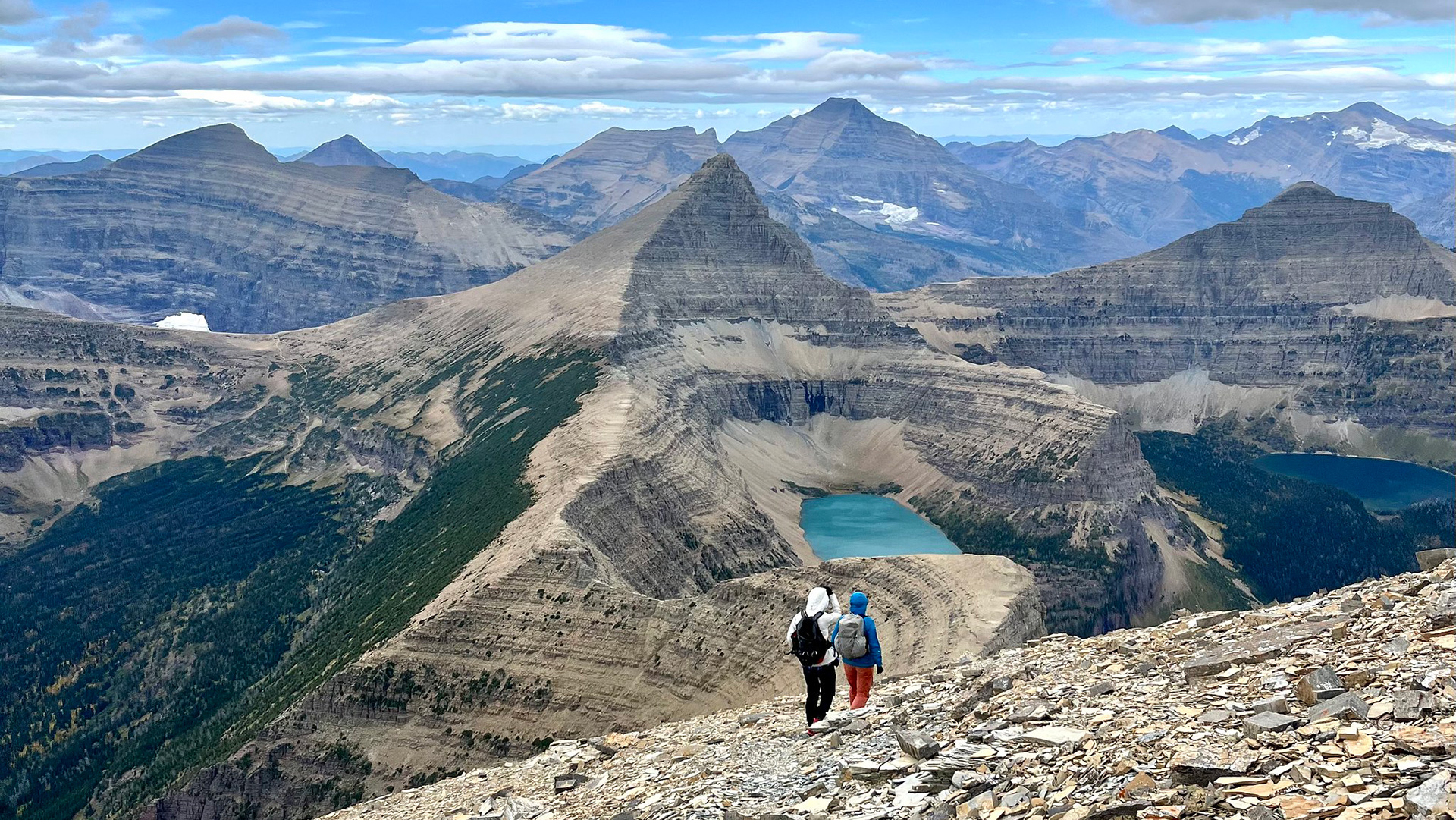 Hikers walking towards a lake with mountains in the background.