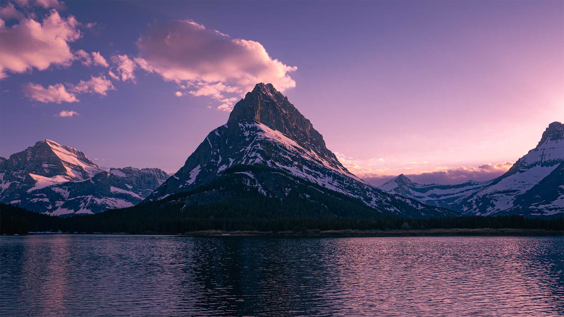 Mountains covered in snow with a purple glowing sky.