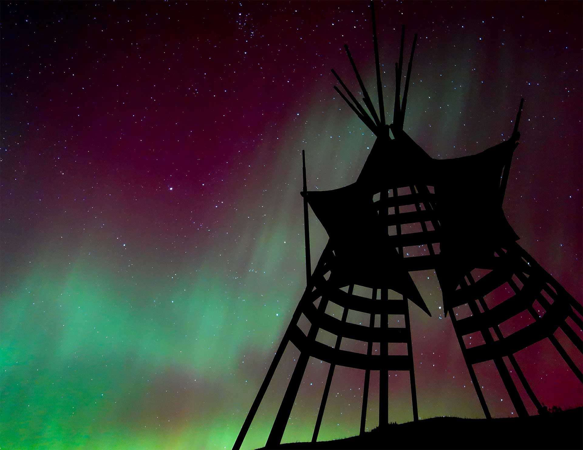 A silouhette of a Blackfeet lodge sculpture with northern lights in the background.