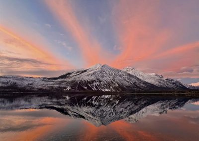 Pink clouds and a snowy mountain reflect on a lake.