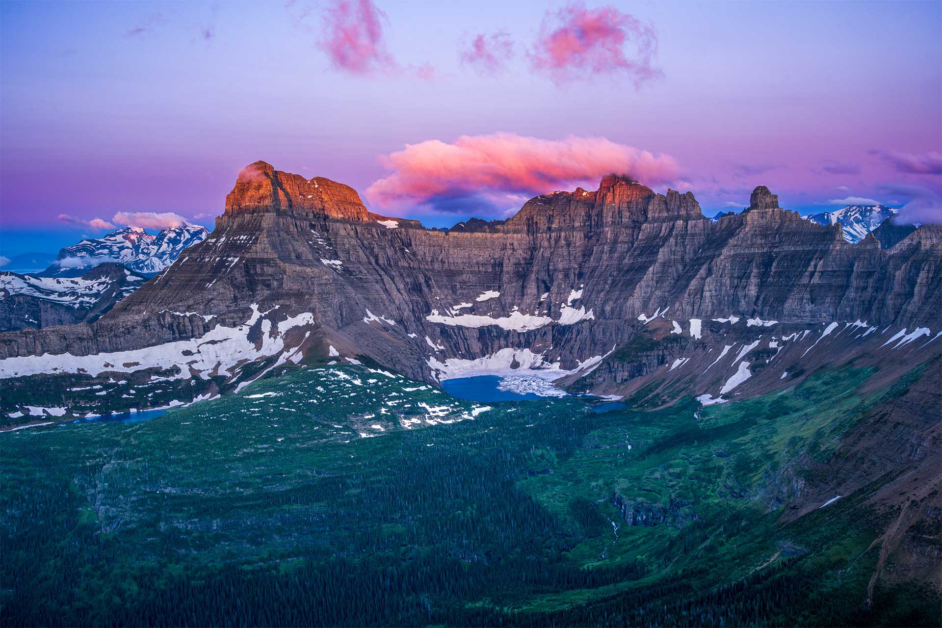 A lake with ice and snow surrounded by mountains at sunrise with a purple sky.