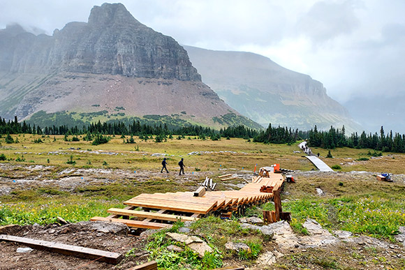 A boardwalk going through an alpine meadow with mountains in the background.