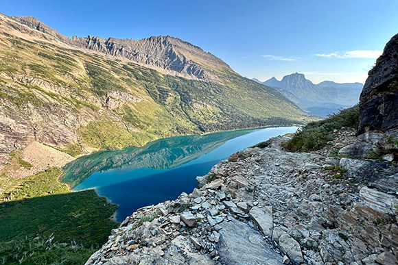 Rocky trail with lake below and mountains in the background.