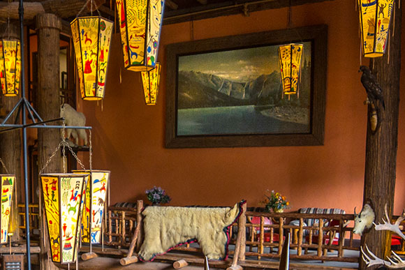 A painting of Avalanche Lake in the lobby of the Lake McDonald Lodge with historic lanterns hanging from the ceiling.