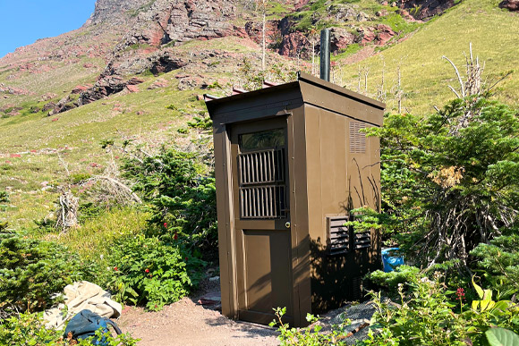 Brown outhouse with mountains in the background.