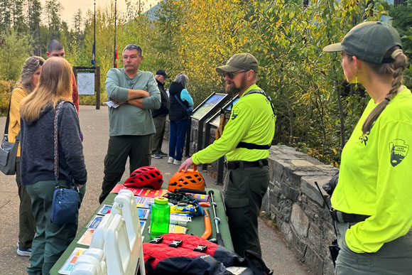 Two park rangers showing visitors climbing helmets and life jackets.